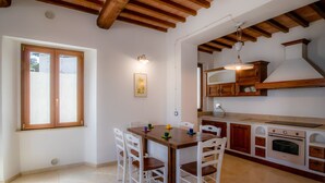 Une cuisine de taille réduite, avec des meubles de rangement en bois, une table à manger avec des chaises et une fenêtre équipée de stores.