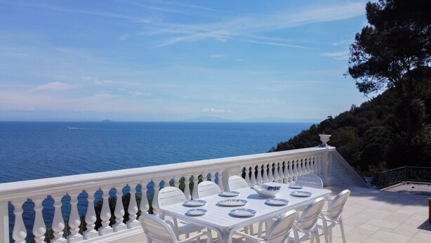 A white outdoor dining area with a view of the sea and a mountainous landscape. - Villa Porticciolo has an heartbreaking view. (Rio Marina)