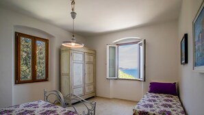 A bedroom with two beds, a wardrobe, a window with a view, and a hanging light fixture. - Villa Porticciolo has an heartbreaking view. (Rio Marina)