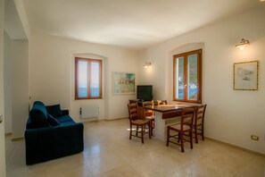 A living room with a blue sofa, a dining table with chairs, a TV, and a window with a view of the sea. - Villa Porticciolo has an heartbreaking view. (Rio Marina)