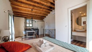 A bedroom with a wooden ceiling, a bed with a red pillow, a rolled-up towel, and a view into the kitchen area. - 1 Bedroom Apartment in Caltagirone (Caltagirone)