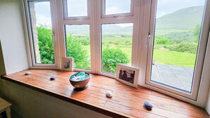 Une baie vitrée à trois vitres, un rebord en bois orné d’un bol et de pierres, et des tableaux encadrés.