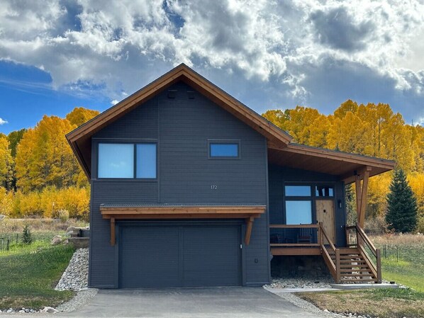 A two-story house with a dark gray exterior, a garage, and a small porch with a staircase. - Summit Sky Ranch | Exclusive Amenities | Kid-Friendly Mountain Home (Silverthorne)