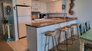 A kitchen with white cabinets, a granite countertop, and a bar area with stools.