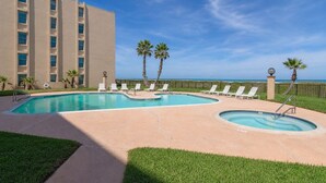 A pool area with lounge chairs, palm trees, and a building with multiple windows.