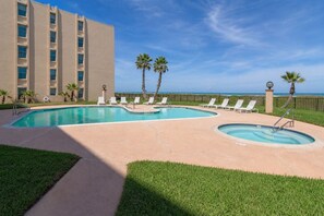 A pool area with lounge chairs, palm trees, and a building with multiple windows.