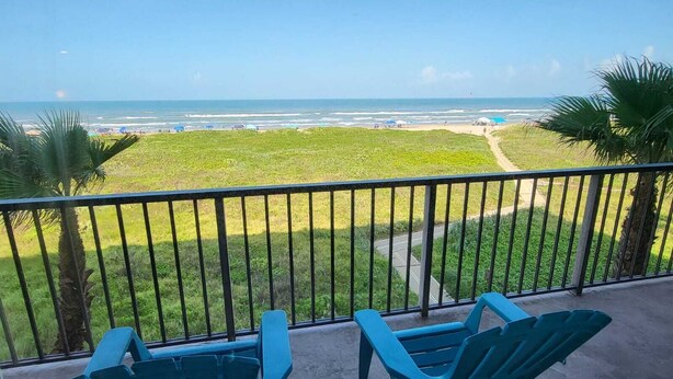 A balcony with two chairs facing a beach view.