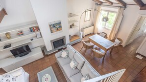 A spacious living area with a fireplace, a dining table with chairs, a sofa with cushions, and a TV on a stand.