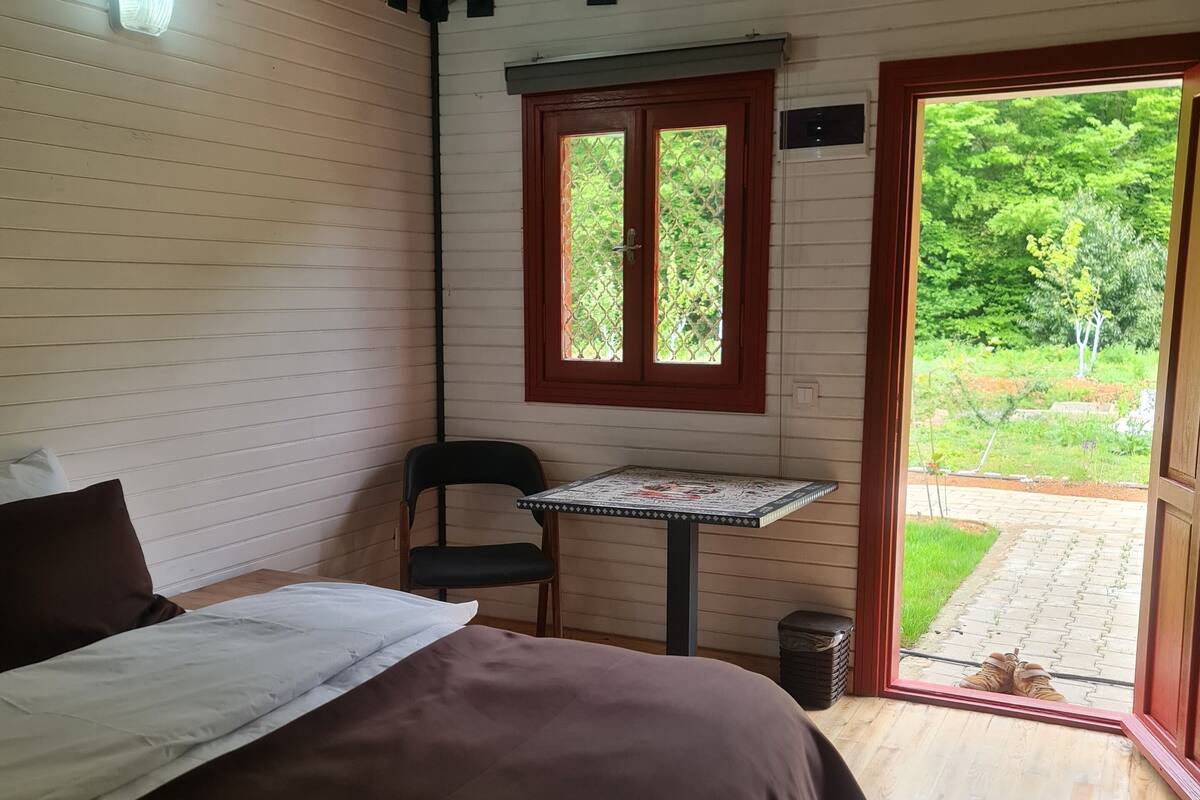 Un dormitorio con cama, una mesita y ventana con vista a un jardín.