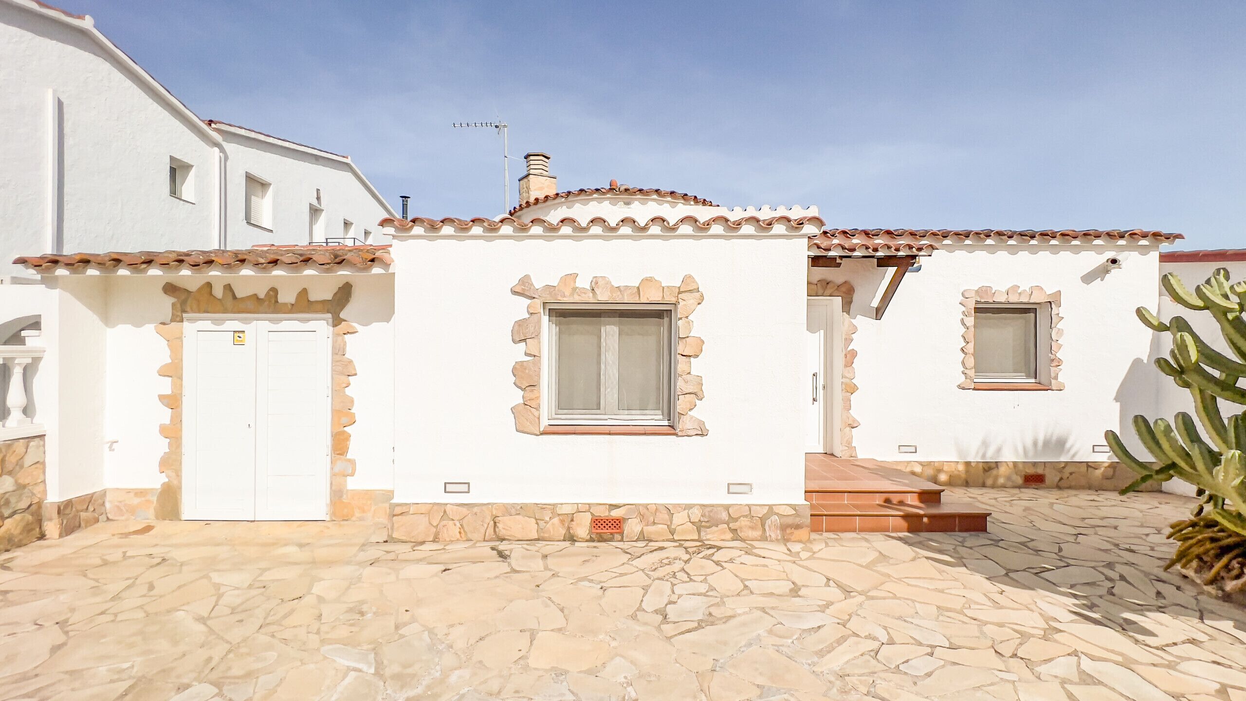 A white building with stone accents, a tiled roof, and two windows with stone frames.