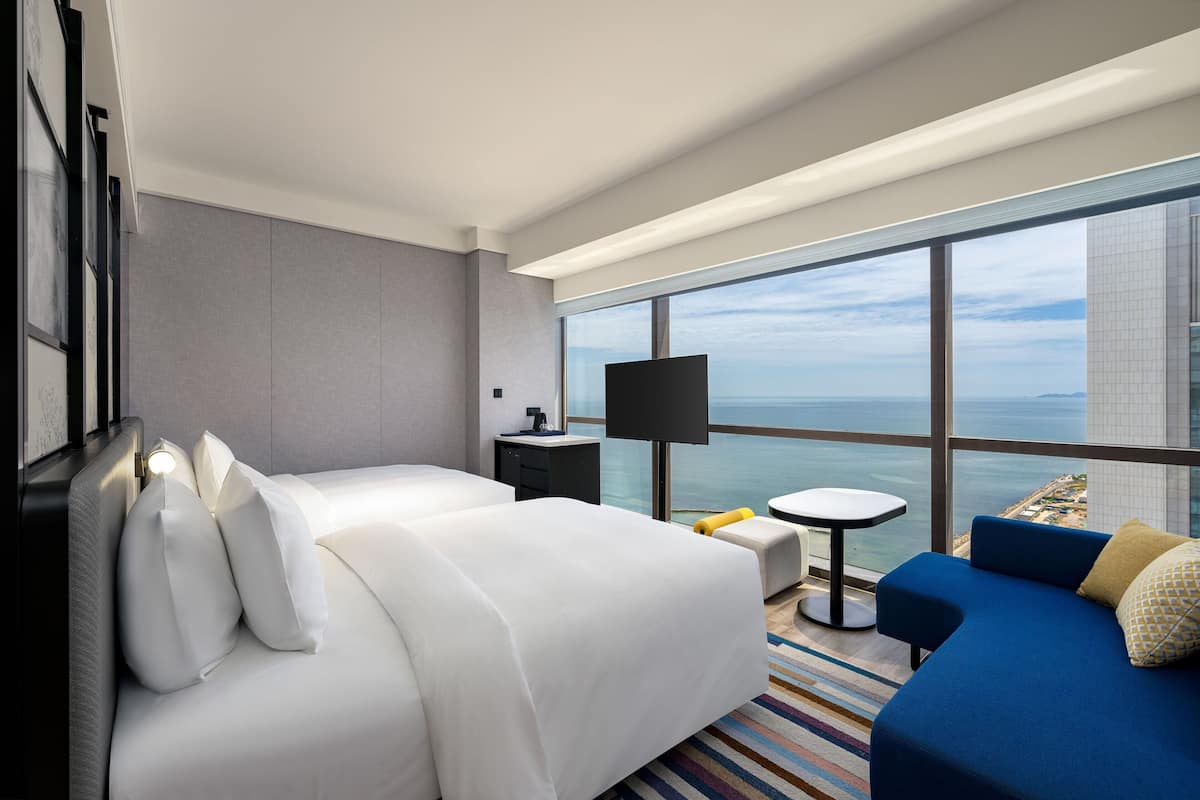 Habitación de hotel con una cama grande, un sofá, una mesita, un televisor y vista al océano.