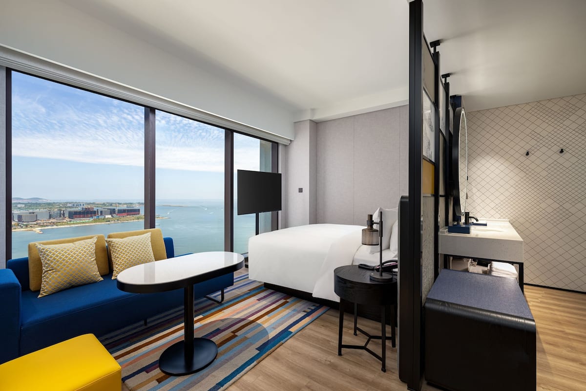 Una habitación de hotel con un ventanal grande, una cama, un sofá, un escritorio y un baño.