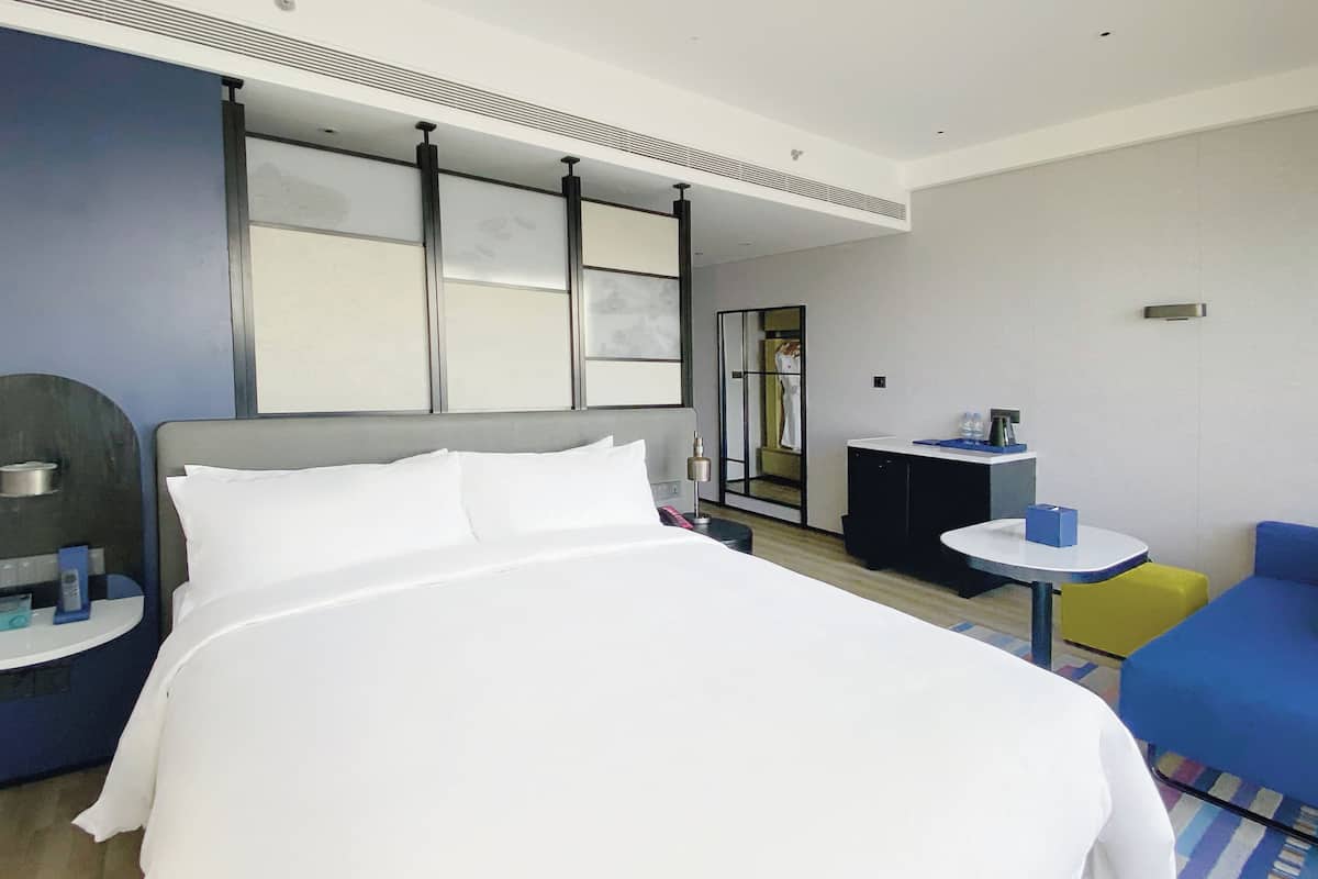 Una habitación de hotel con una cama grande, un escritorio pequeño, una silla, un sofá y un espejo.