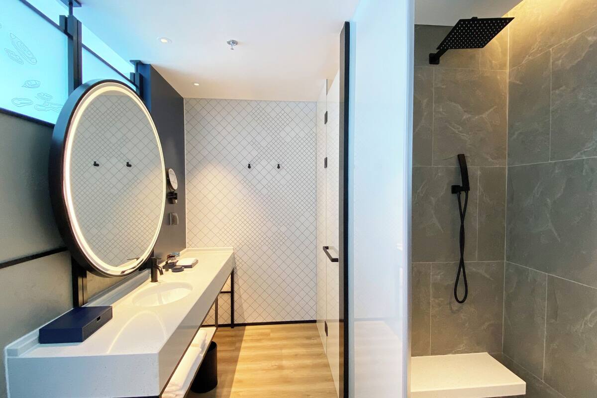 Un baño moderno con un espejo grande, un lavamanos y una ducha.
