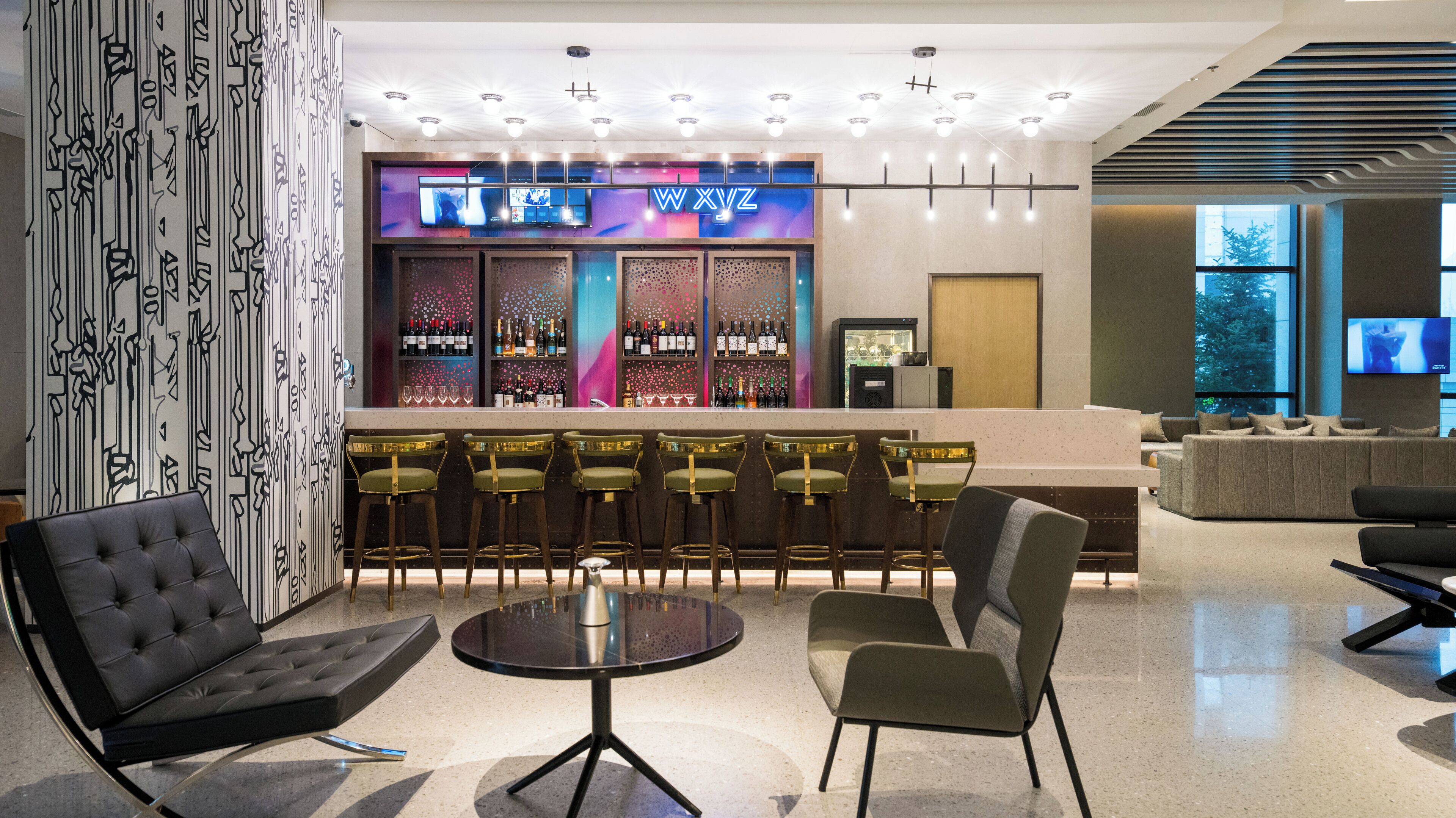 A modern bar area with a bar counter, multiple stools, and a seating area with a sofa and chairs.