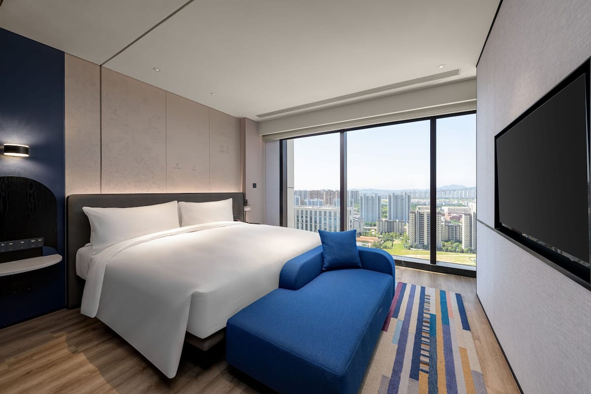 Habitación de hotel moderna con una cama grande, un sofá, un televisor de pantalla plana y vista a la ciudad.