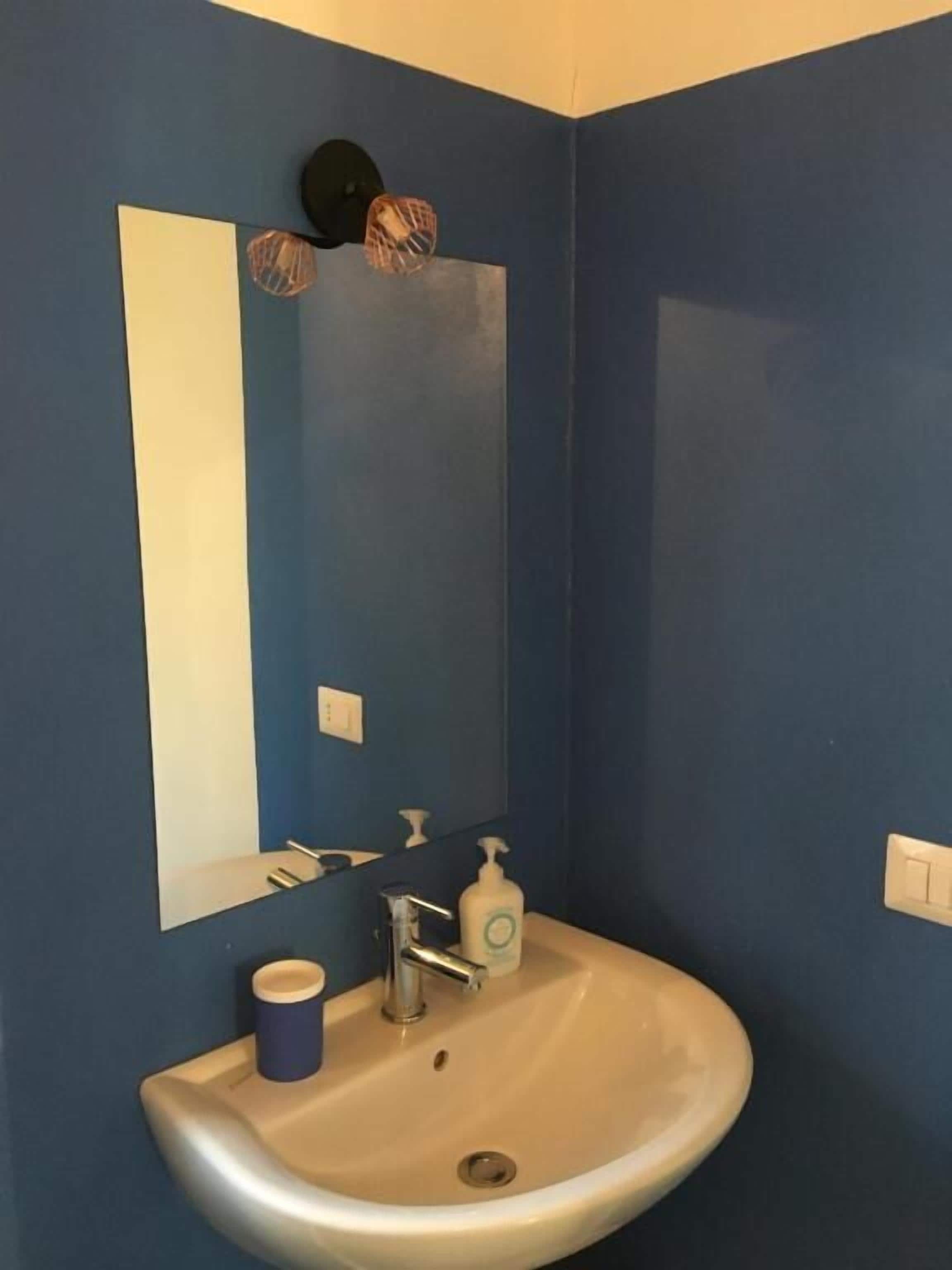 A bathroom with a white sink, a mirror, a blue wall, and a black hat hanging on the wall.