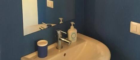A bathroom with a white sink, a mirror, a blue wall, and a black hat hanging on the wall.