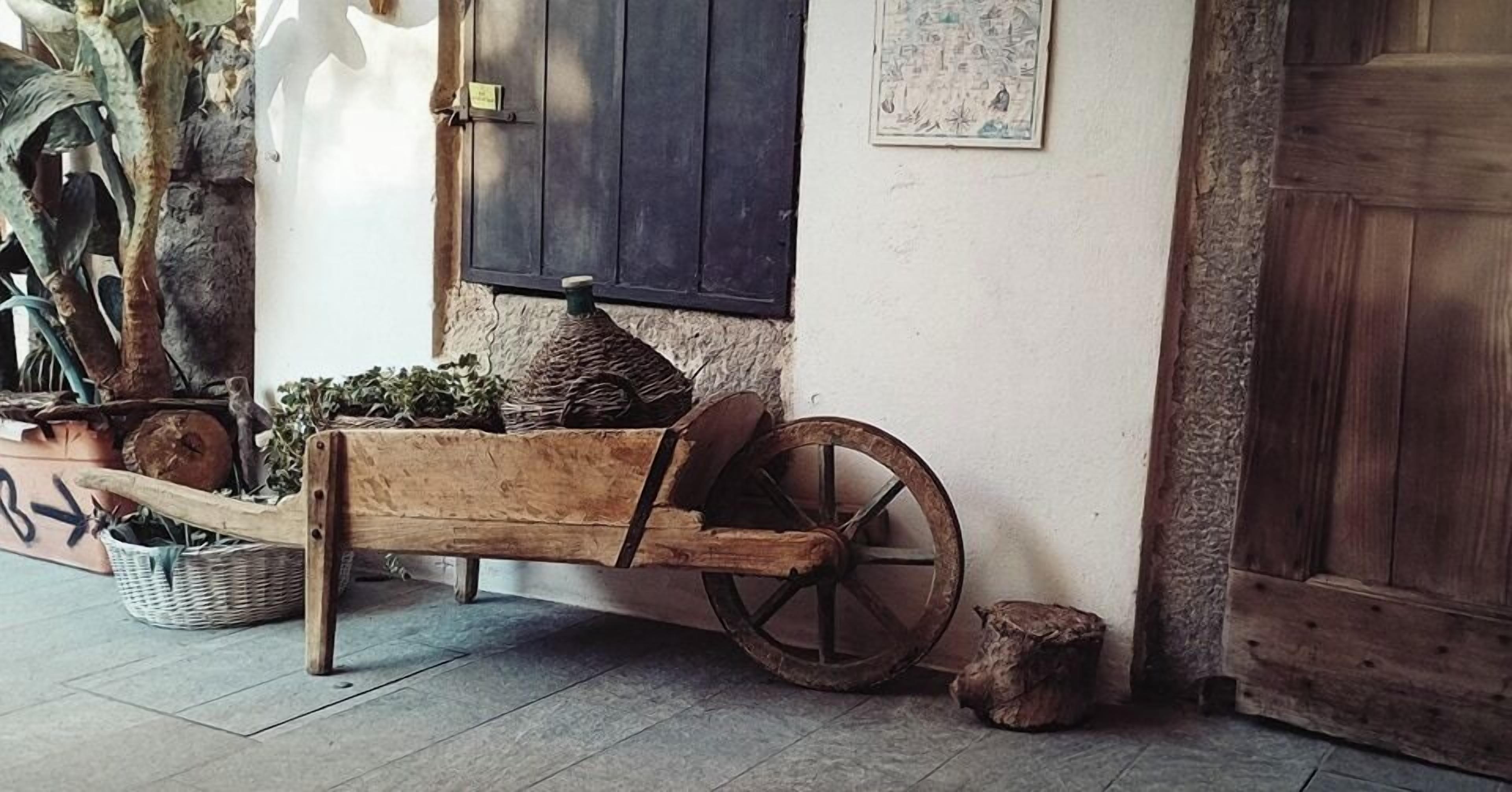 Una panca di legno rustica con una ruota, un cesto di vimini e uno sgabello in legno, il tutto in un ambiente tradizionale.