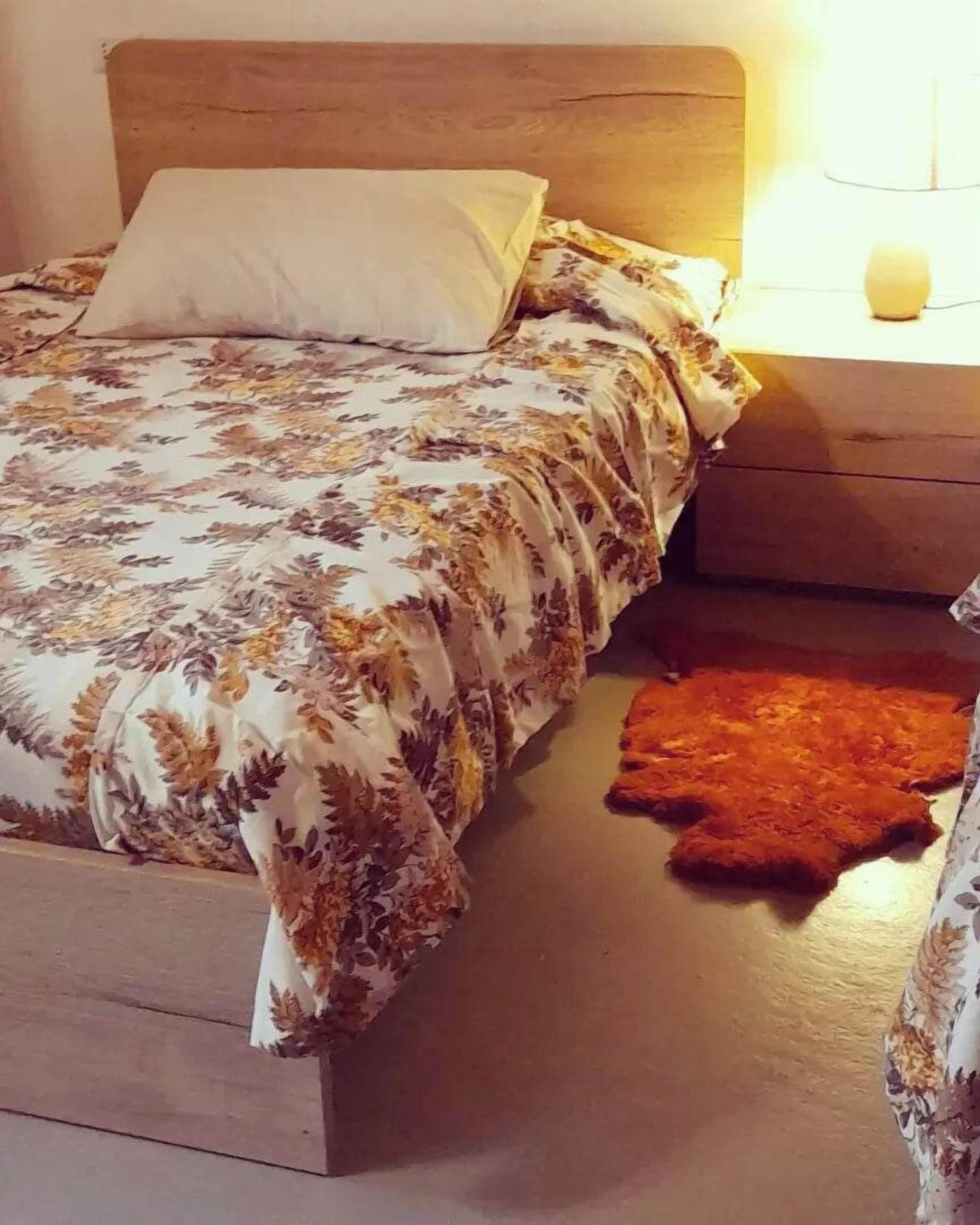 Ein Bett mit floralem Überwurf, einem Holzkopfende, einer Nachttischlampe und einem kleinen Teppich auf dem Boden.