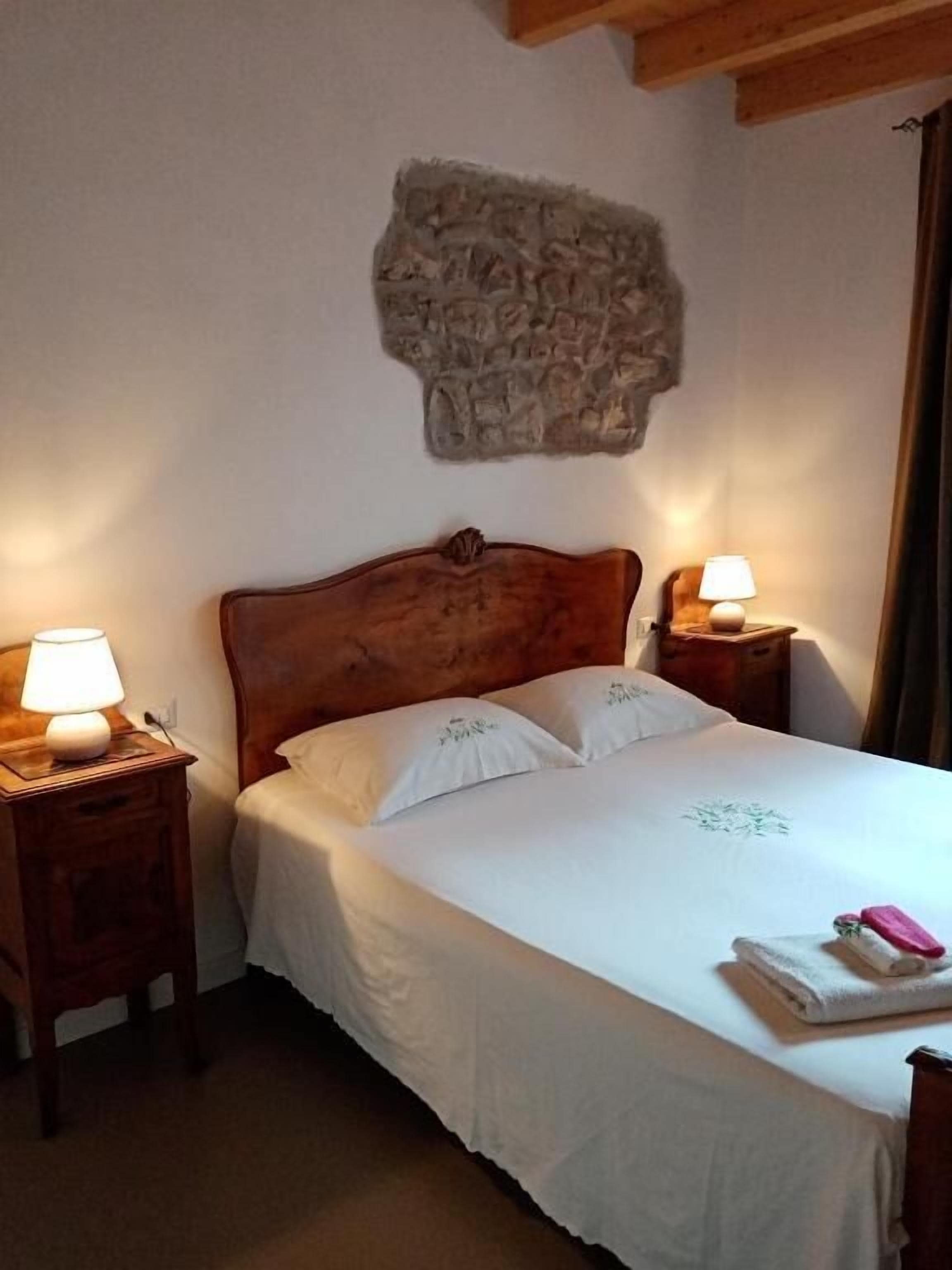 Una cama bien hecha con sábanas blancas, dos lámparas de noche y un adorno de pared de piedra encima.