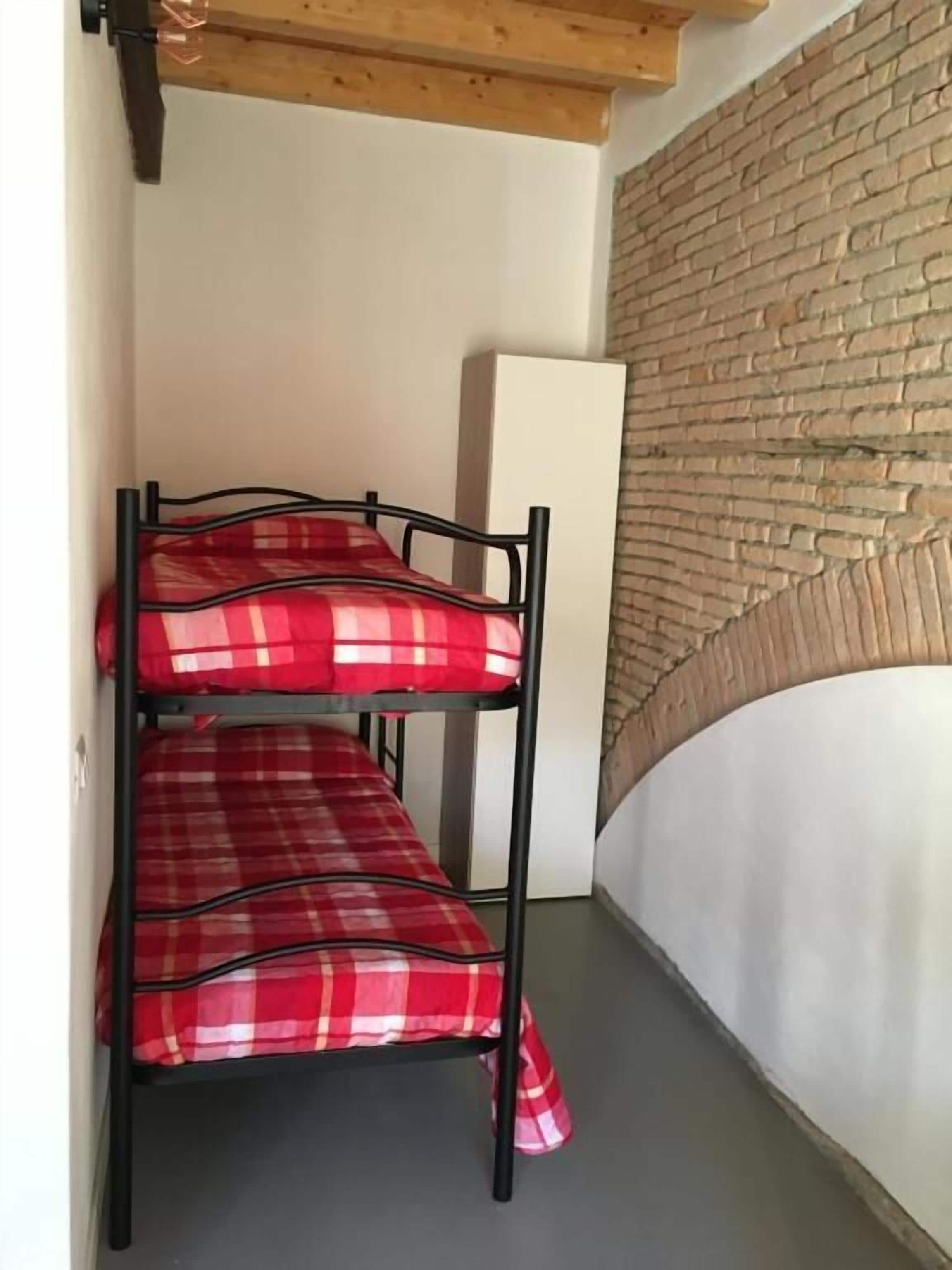 A bunk bed with red plaid bedding in a room with a brick wall and a white cabinet.