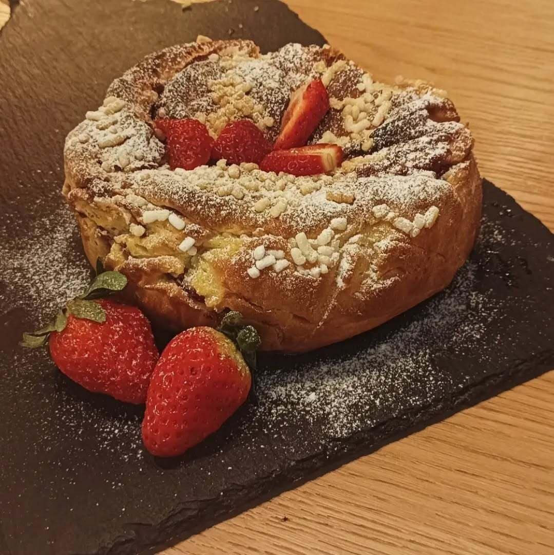 Ein Dessert mit Erdbeeren und Puderzucker auf einer Schieferplatte.