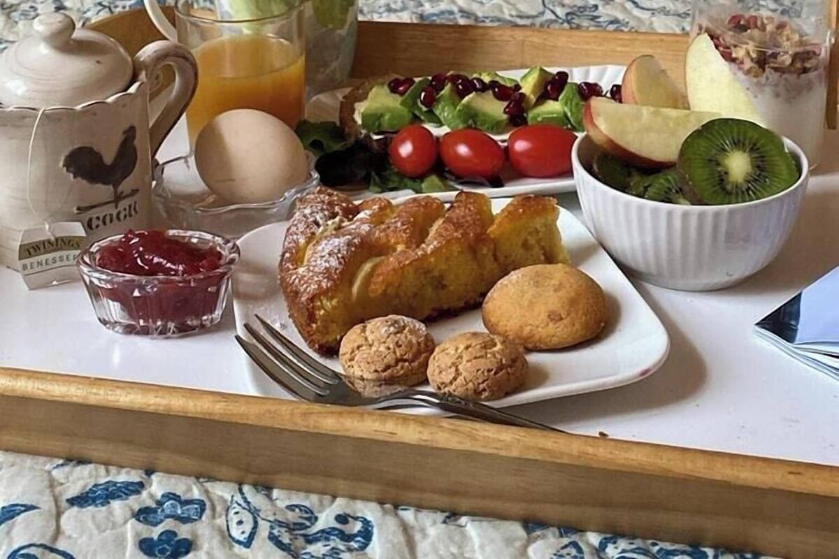 Un plateau de petit-déjeuner avec des croissants, des muffins, une salade, des fruits et une tasse, posé sur un lit recouvert d’une couverture à motifs floraux.