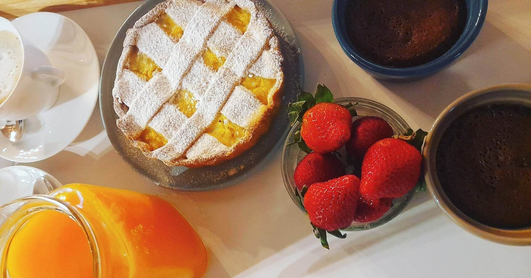 En morgenmadsopstilling med en frugttærte, jordbær, kaffe og appelsinjuice.