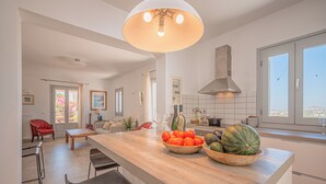 A modern kitchen with a central island, bar stools, and a dining area with a red chair.