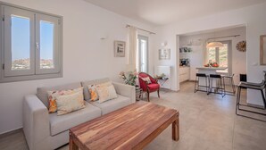 Ein geräumiges Wohnzimmer mit einer Couch, einem Holztisch und einem roten Sessel. Es gibt eine Küchenzeile mit einem Esstisch und Barhocker.