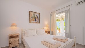 A bedroom with a bed, bedside tables, a painting, and an open door leading to an outdoor area.