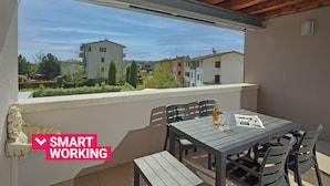Un balcon avec une table et des chaises, une statue et une vue sur les bâtiments.