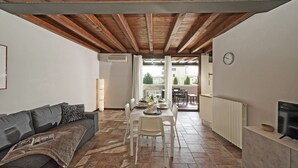 Un salon comprenant un canapé, une table à manger et des chaises. On y trouve également un téléviseur posé sur un meuble et une fenêtre avec des rideaux.
