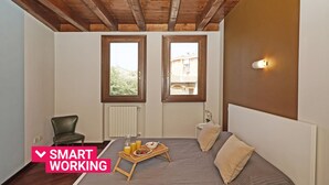 Une chambre à coucher comprenant un lit, une chaise, une table de chevet, une commode, une fenêtre et un luminaire fixé au mur.