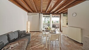 Un coin repas avec une table dressée pour deux personnes, un canapé et une horloge au mur.