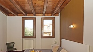 Ein Schlafzimmer mit Bett, Sessel, Nachttisch, Fenster und einer Wandleuchte.