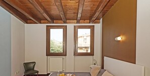 Une chambre à coucher comprenant un lit, une chaise, une table de chevet, une commode, une fenêtre et un luminaire fixé au mur.