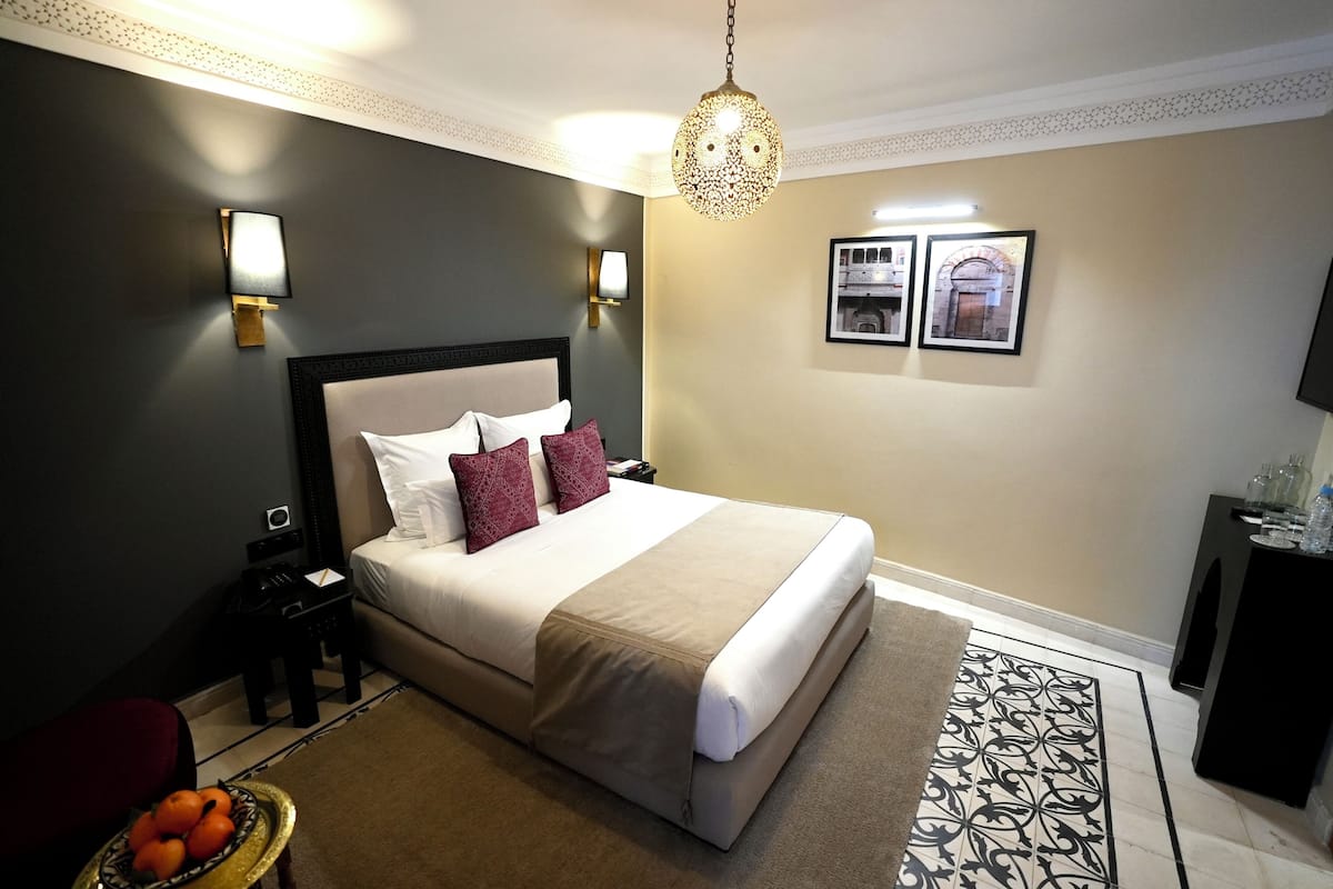 Habitación de hotel con una cama grande, mesitas de noche, una lámpara, un adorno en la pared y una pequeña mesa con un frutero.
