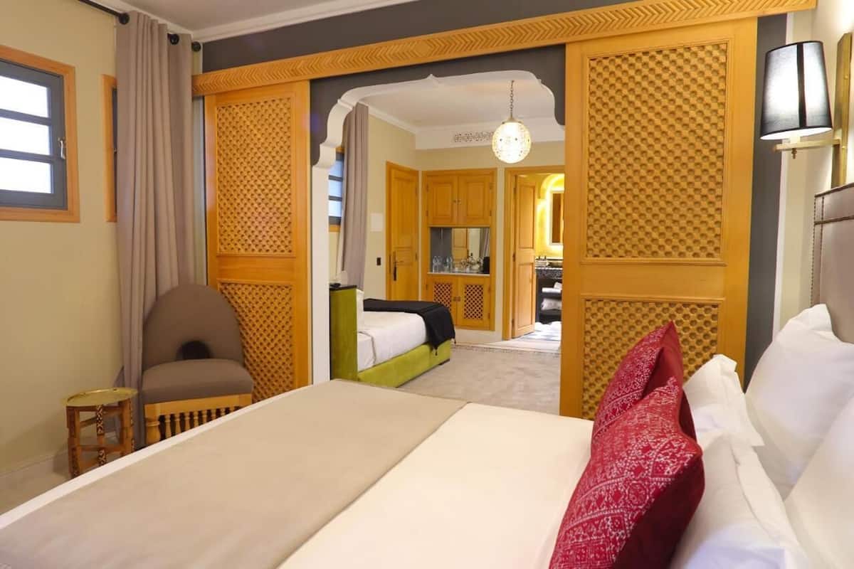 Habitación de hotel con una cama grande, una silla, una mesita pequeña y una kitchenette al fondo.