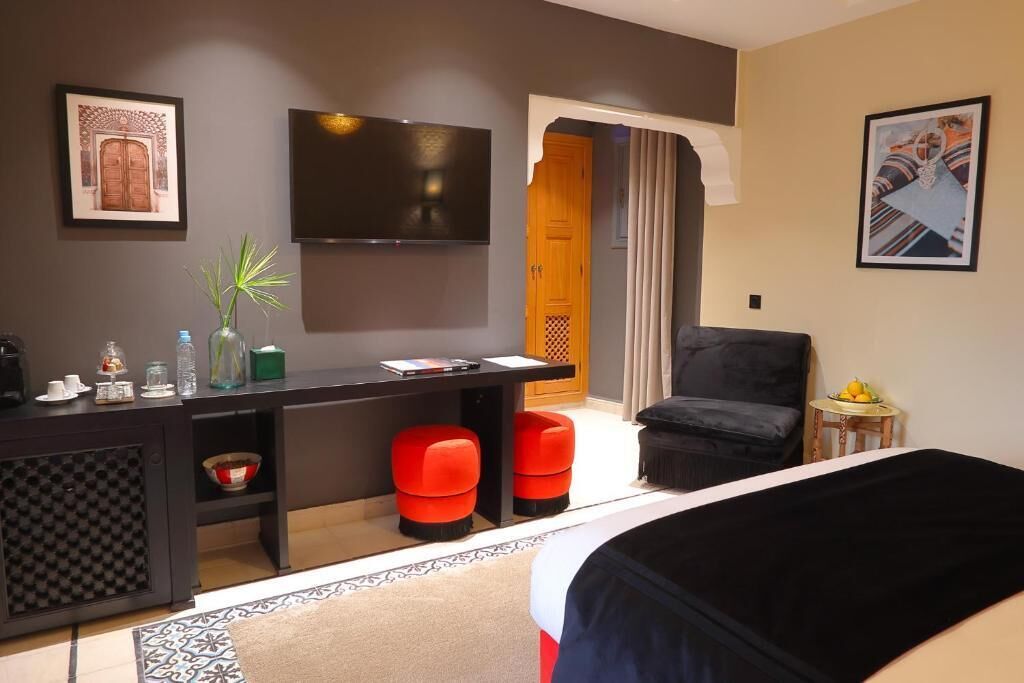 Een moderne hotelkamer met een bed, een bureau met een flatscreen televisie, een stoel en een kleine tafel met fruit.