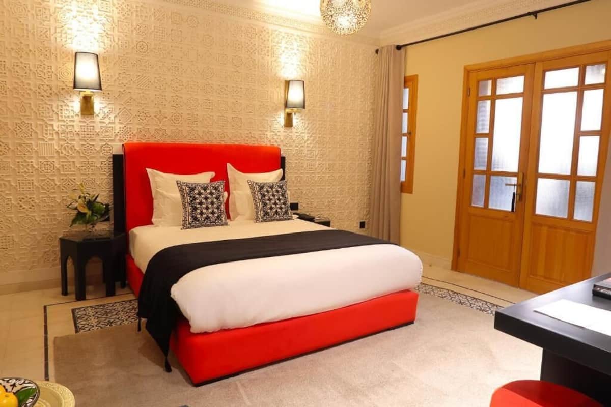 Un dormitorio con cama roja, pared estampada, dos lámparas de noche y una puerta de madera.