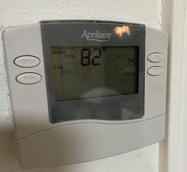 Un termostato fijado a la pared con pantalla digital que muestra la temperatura de 82°F, marca Aprilaire.
