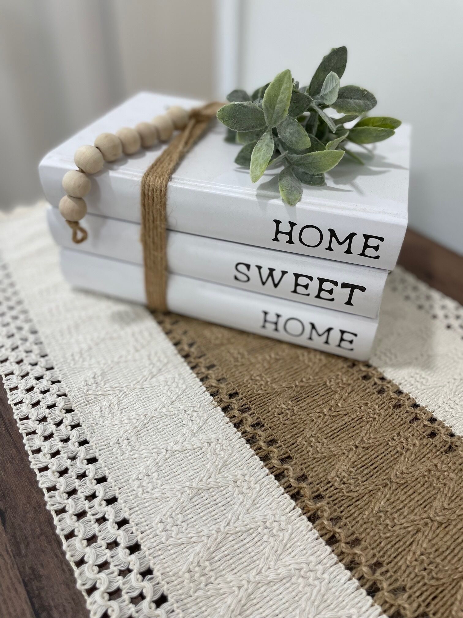 A stack of white blocks with "HOME SWEET HOME" written on them, tied with a brown string and a small green plant on top.