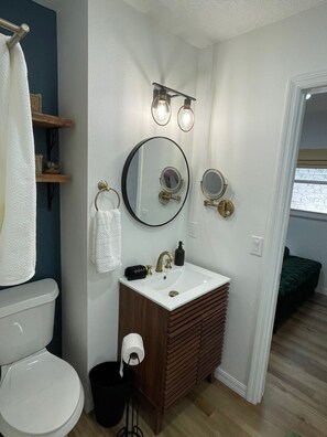 A bathroom with a toilet, sink, and two mirrors. There are shelves above the sink and a towel rack to the left.