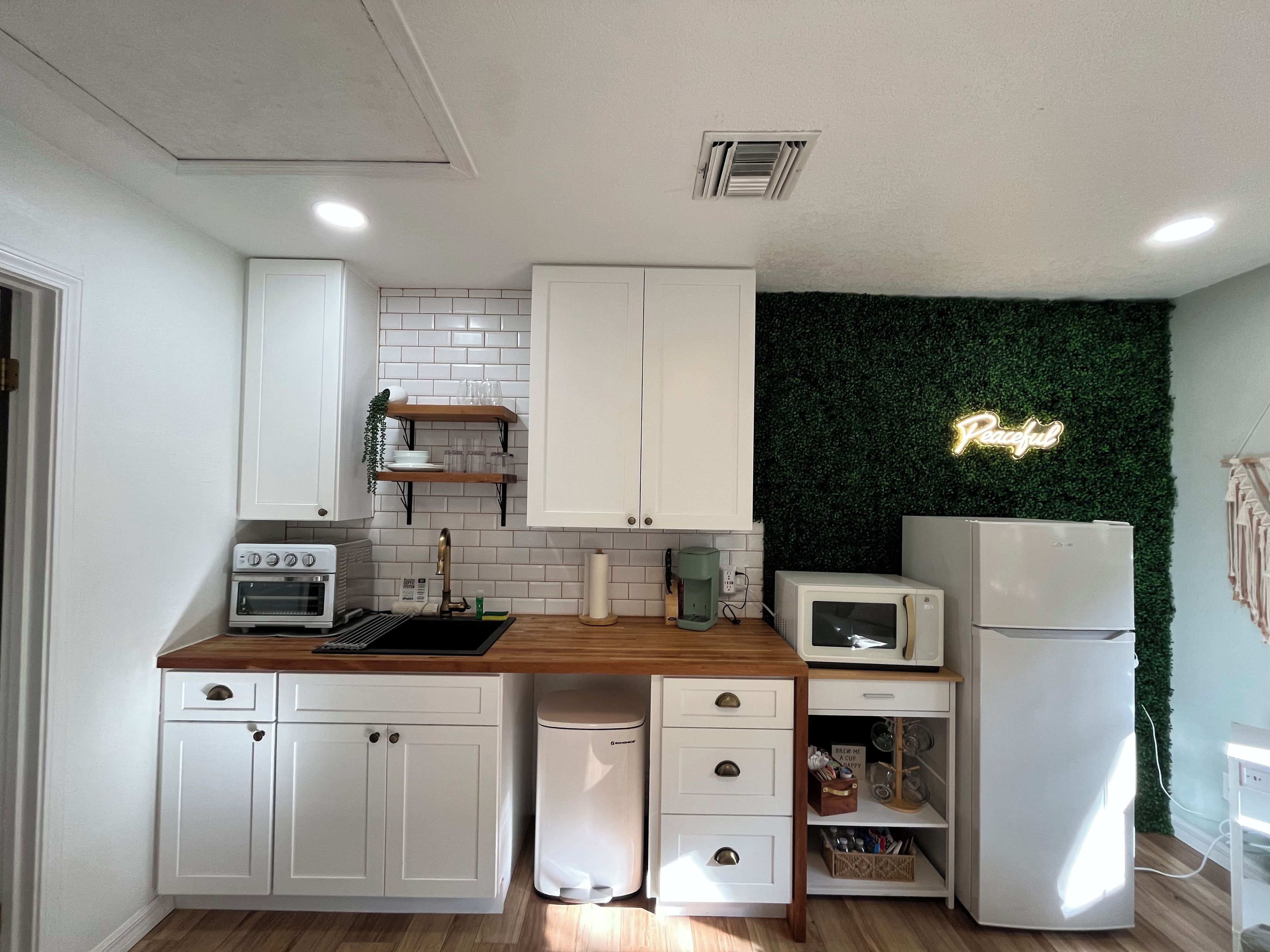 A modern kitchen with white cabinetry, a built-in microwave, a coffee maker, and a neon 'Peaceful' sign on the wall.