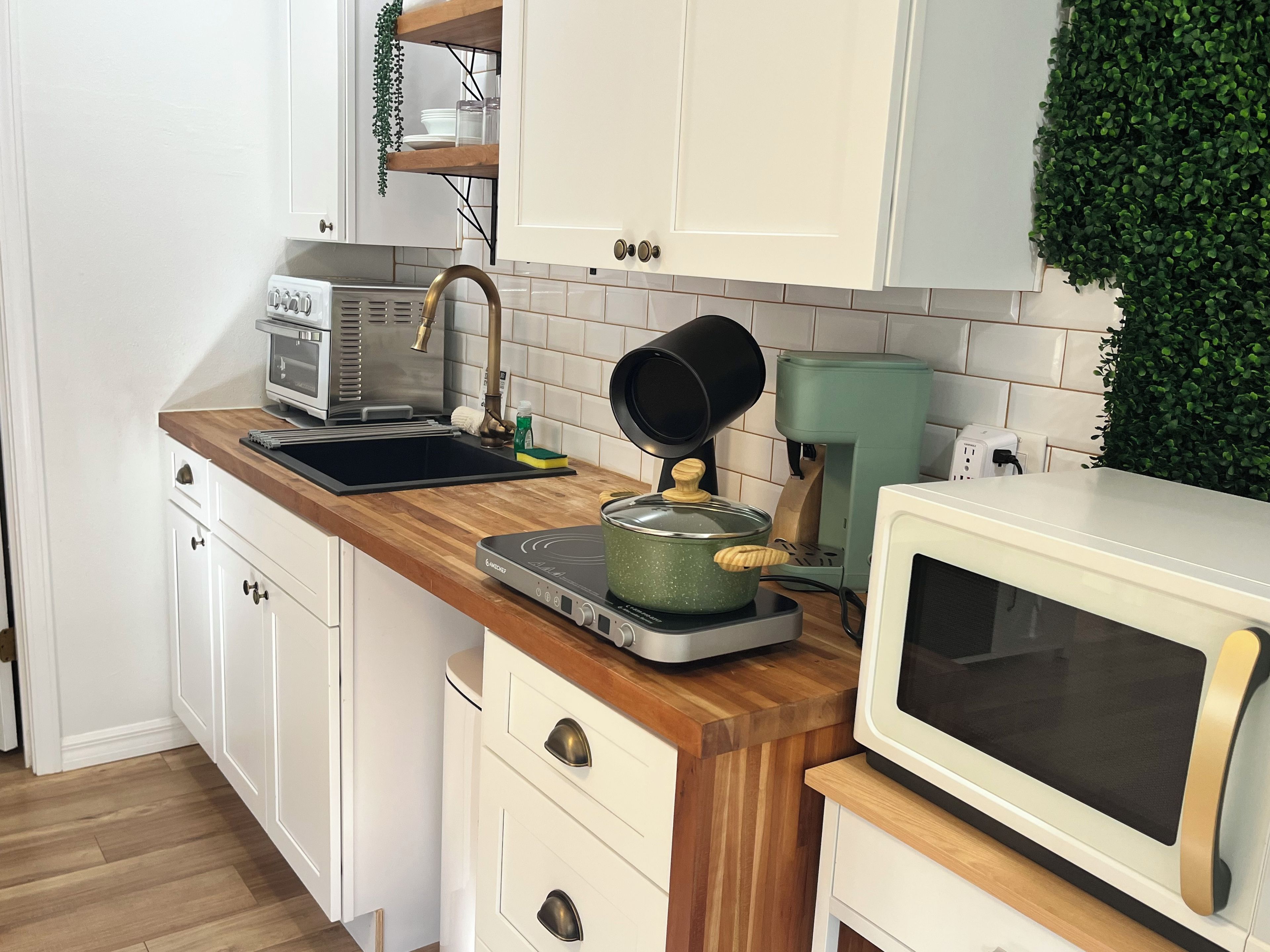 A kitchen with white cabinets, a wooden countertop, a stove, a microwave, and a coffee maker.