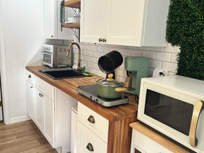 Eine Küche mit weißen Schränken, einer Holzarbeitsplatte, einem Herd, einer Mikrowelle und einer Kaffeemaschine.