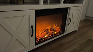 Un mueble blanco con chimenea empotrada, suelo de madera y un estante con objetos decorativos.