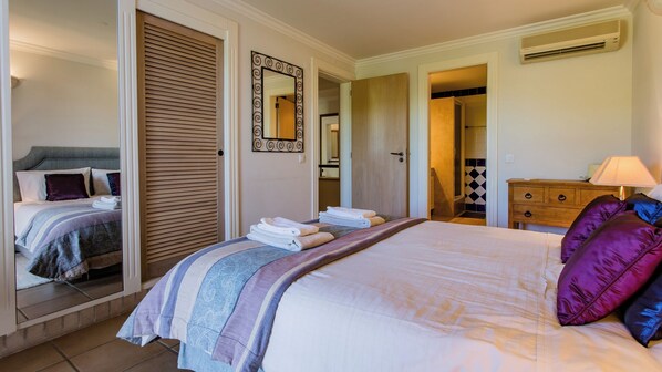 A hotel room with a bed, a wooden wardrobe, a mirror, a nightstand, and a bathroom visible through an open door.